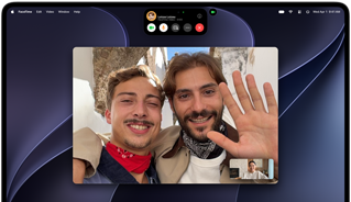 MacBook Pro with PROLED XDR Display, silver color, display shows a video call in progress with two people in a sunlit town waving to a person at home